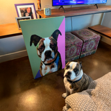 Dog sitting next to a painting of itself in a home setting