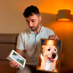 Man holding a framed photo of a dog with a warm indoor setting